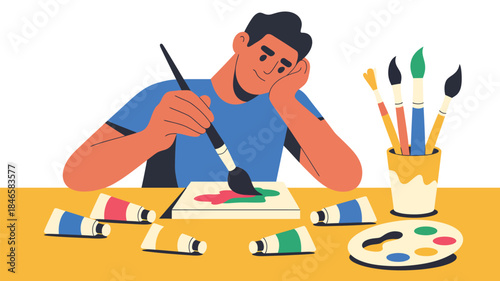 Creative man painting with colorful brushes and tubes around