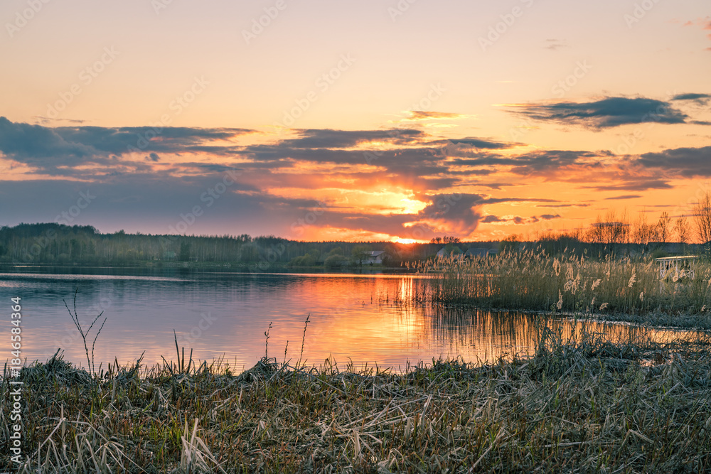 Fototapeta premium Beautiful sunset over a lake with a small house in the distance