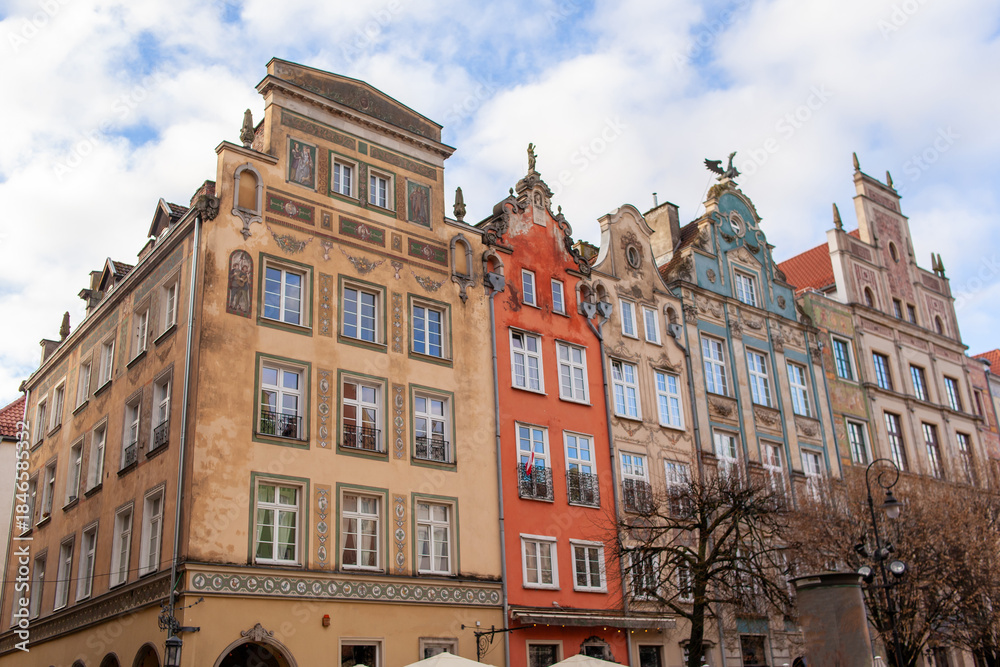 Fototapeta premium Old buildings with different colors sit next to each other on a busy street in a city known for its history. The sky is cloudy. A cobblestone street in Gdansk, Poland