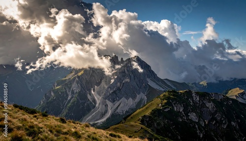 Dramatic mountain landscape under fluffy clouds, with a green hillside in the foreground