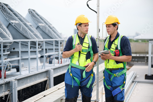 Two construction workers on a rooftop discussing a project, dressed in safety gear and hard hats