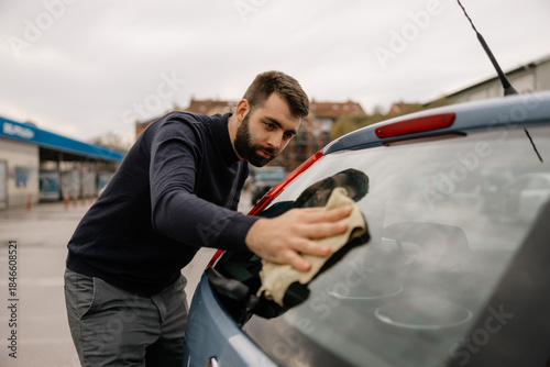 Auto detailing worker cleaning car window by hand