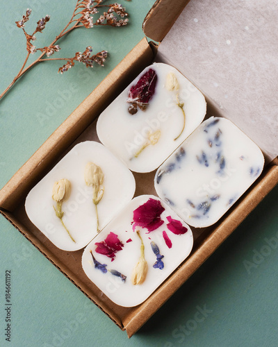 Four Florentine wax sachets beautifully arranged in a cardboard gift box on a light green background. Each sachet contains different dried flowers 