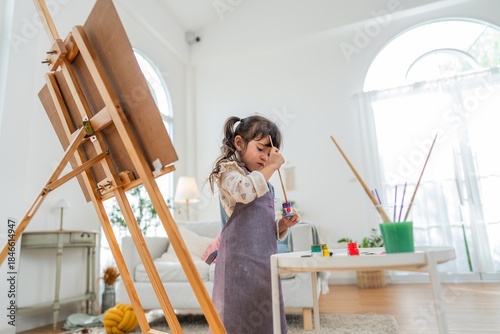Child paints at home in bright room with easel and art supplies during afternoon activity