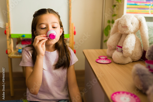 Slika na platnu Little girl playing pretend serving tea to stuffed animal bunny during imaginati