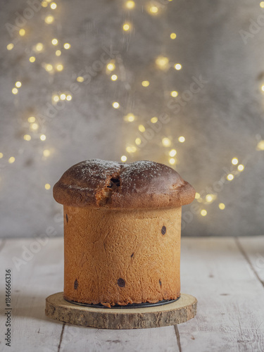 Vertical image of an isolated panettone, Christmas lights with bokeh effect in the background, on a white wooden table with free space for text