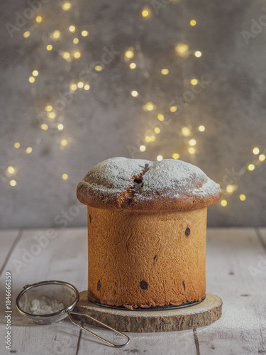 Vertical image of an isolated panettone, Christmas lights with bokeh effect in the background, on a white wooden table with free space for text