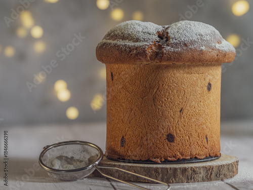 Horizontal image of an isolated panettone, Christmas lights with bokeh effect in the background, on a white wooden table with free space for text