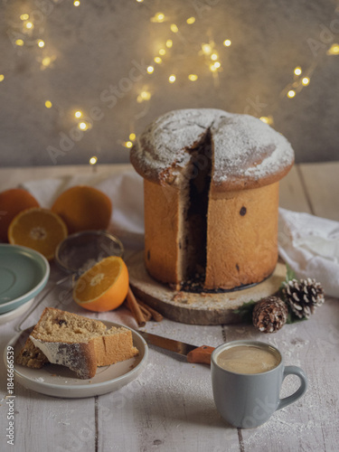 A slice of traditional Italian panettone next to a cup of coffee on a wooden table with Christmas lights. Space for text