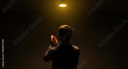 Person Clapping Beneath a Soft Yellow Light in a Dark Space, Expressing Emotion and Joy