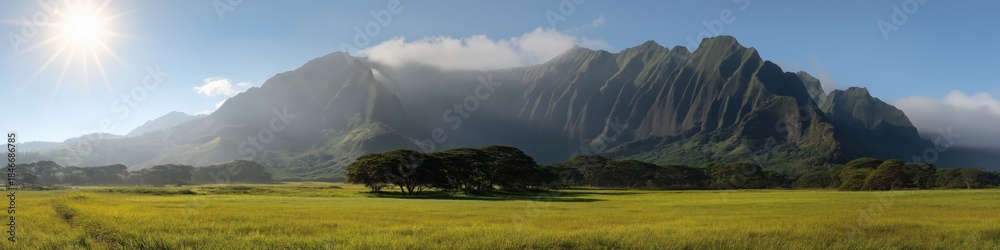 Obraz premium Majestic mountain range under clear blue sky with lush green meadow and sunburst