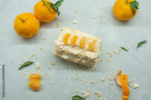 A delicious meringue roll with fruit. A top view of the meringue cake and tangerines against a gray background.