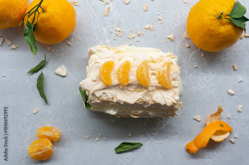 A delicious meringue roll with fruit. A top view of the meringue cake and tangerines against a gray background.
