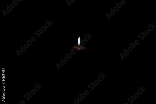 Świeca płonąca w całkowitych ciemnościach. Widoczny jest tylko płomień i górna część świecy.