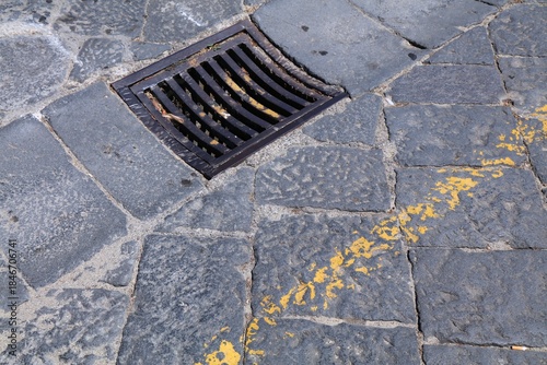 Fototapeta Naklejka Na Ścianę i Meble -  Rainwater drain cast iron metal grate - urban infrastructure in Messina, Italy. Old cobblestone street pavement.