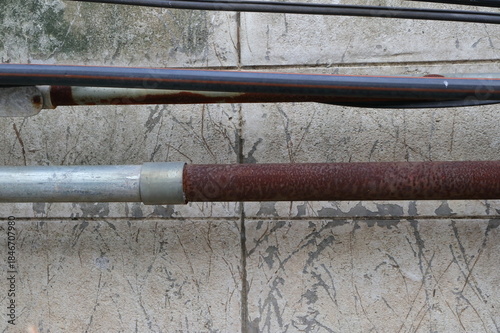 Metallic pipe transitions from a clean, silver finish to a rusted surface joined by a metal coupling. The background wall is a textured, light gray surface marked with dark streaks and peeling paint.
