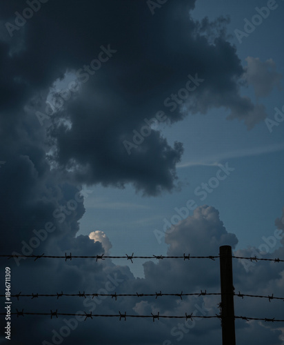 Barbed wire fence under dramatic dark clouds at twilight, Day of Remembrance for the Victims of Genocide in World War II  