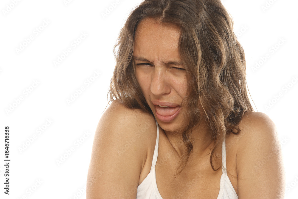 Fototapeta premium Studio shot of a young woman with long brown hair and no makeup, disgusted expression with tongue out, portrait, on a white background