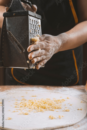 Chef grating cheese into dough in restaurant kitchen .