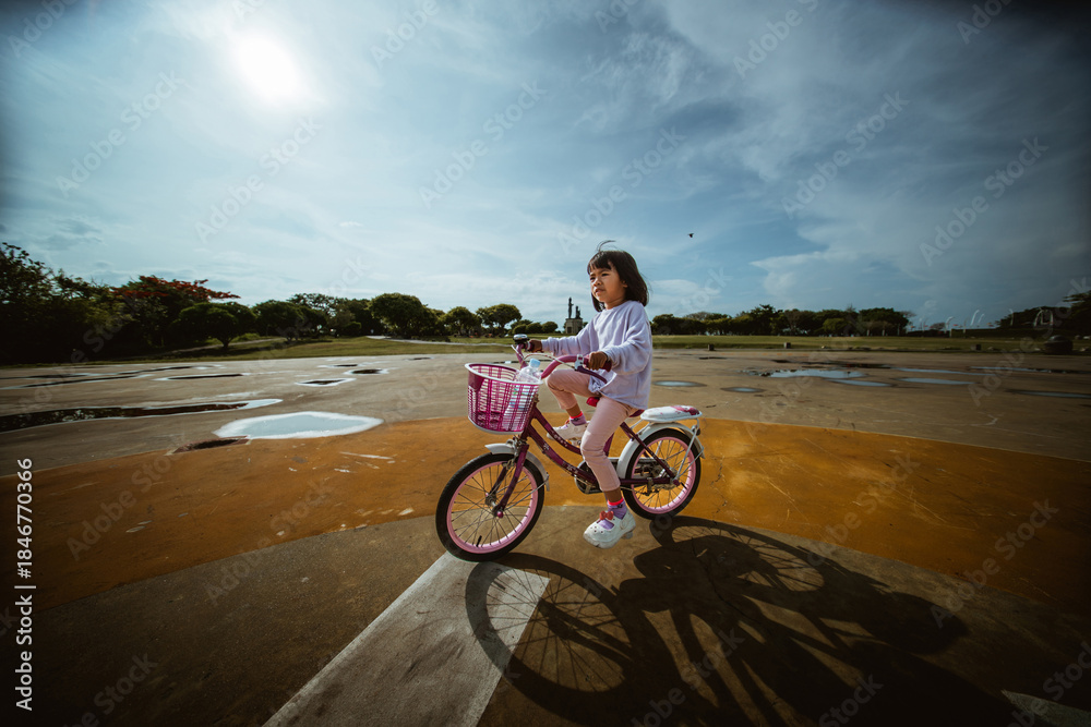 Fototapeta premium A happy girl is enjoying riding a colorful bicycle on a beautiful sunny day