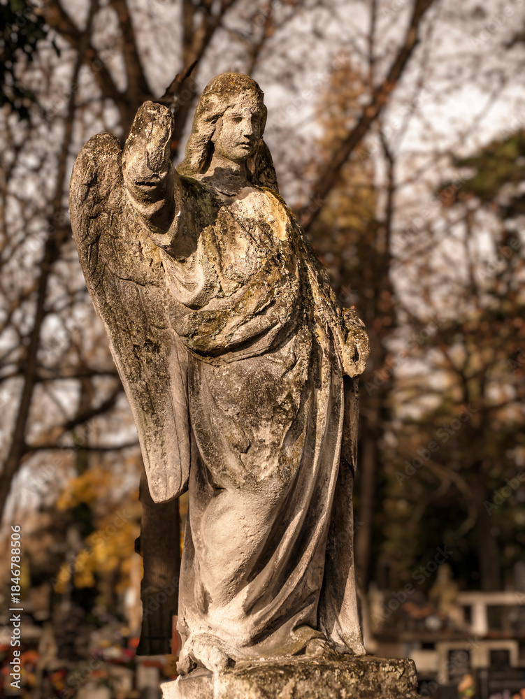 Fototapeta premium Weathered Angel Statue Guards a Quiet Graveyard Under Ancient Autumn Light