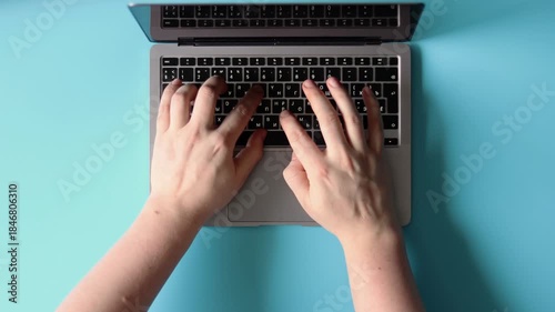 Hands typing on a laptop keyboard against a blue background. Flatlay concept, advertising remote work
