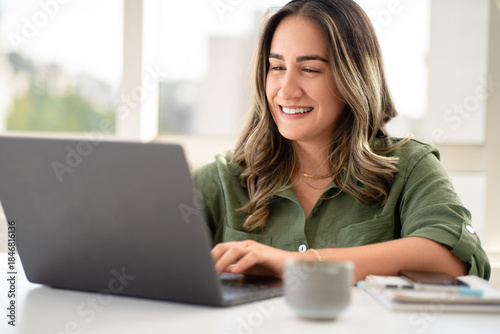 Quadro em tela Cheerful Latin businesswoman in her 30s wearing olive green shirt working on lap