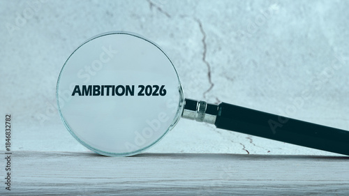 Quadro su tela A magnifying glass rests on a surface, focused on the phrase Ambition 2026, brin