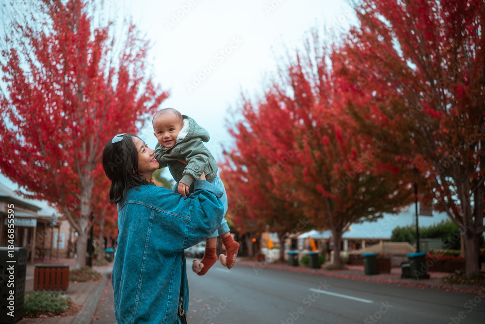 Fototapeta premium A joyful mother lovingly holds her baby amid the stunning autumn foliage and colors