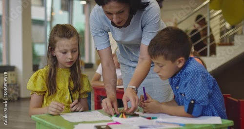 Creative kids during an art class in a daycare center or elementary school classroom drawing with female teacher. 