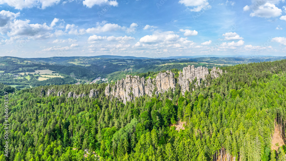 Naklejka premium Explore the stunning sandstone formations of Suche skaly in Bohemian Paradise, surrounded by lush forests and rolling hills under a bright blue sky.