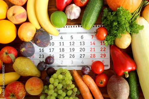  There are a lot of fresh vegetables and fruits on a calendar sheet on a wooden table.