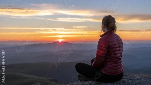 Serene woman meditates during breathtaking mountain sunset with vibrant orange sky