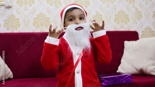 cute baby santa posing with beard on red sofa indoors
