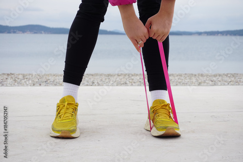 Outdoor resistance band leg exercise on beach in cold weather, legs in sneakers front view, simple daily workout, everyday training, balance, mobility, wellness routine. Healthy habits.
