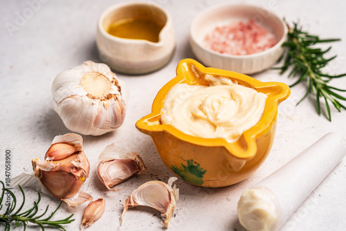 Homemade aioli or allioli garlic sauce in a special mortar on a table with the pestle on the side and ingredients the garlic, olive oil and salt