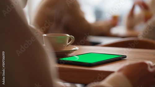 Over the Shoulder View of Hand Swiping Green Screen Tablet in Cafe with Steaming Coffee
