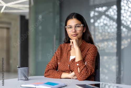 Quadro su tela Young south asian businesswoman with glasses sitting at her office desk, looking