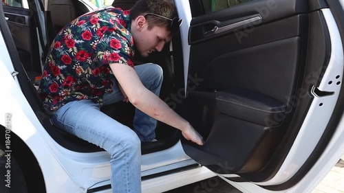 A man wipes the passenger door of a car with a napkin at a car wash.