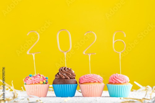 Homemade muffins decorated with 2026 numbers on yellow background. Happy New Year, Merry Christmas concept.