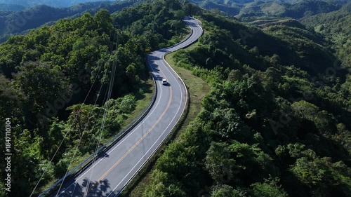 Aerial view highway Drone flying above winding road during sunlight, Winding asphalt road through tropical rainforest. countryside landscape. Landmark tourist attractions in Nan Province, Thailand.	