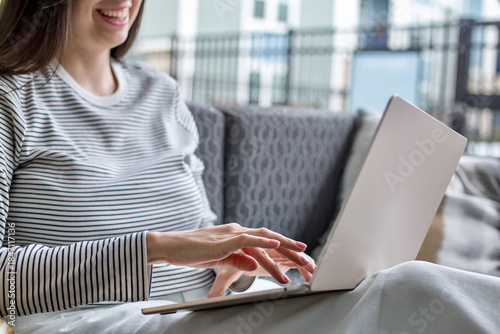 Smiling woman typing on a laptop while relaxing on a sofa, illustrating remote work, online tasks, productivity and modern digital lifestyle in a cozy outdoor-home setting with natural light.