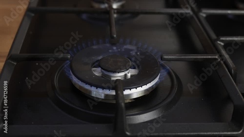A gas burner lights up with a blue flame on a stovetop for cooking food