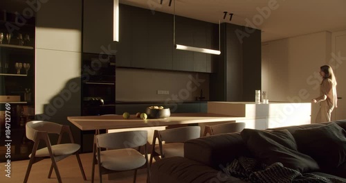 Modern kitchen interior with dark green cabinets, white countertop, and wooden dining table. Sunlight streams through the window, illuminating the room.