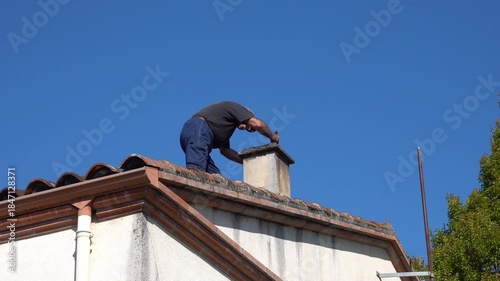 A chimney sweep on a roof removes dust from the surface of a chimney