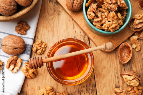 Foto Delicious honey in glass bowl, dipper and walnuts on wooden table, flat lay