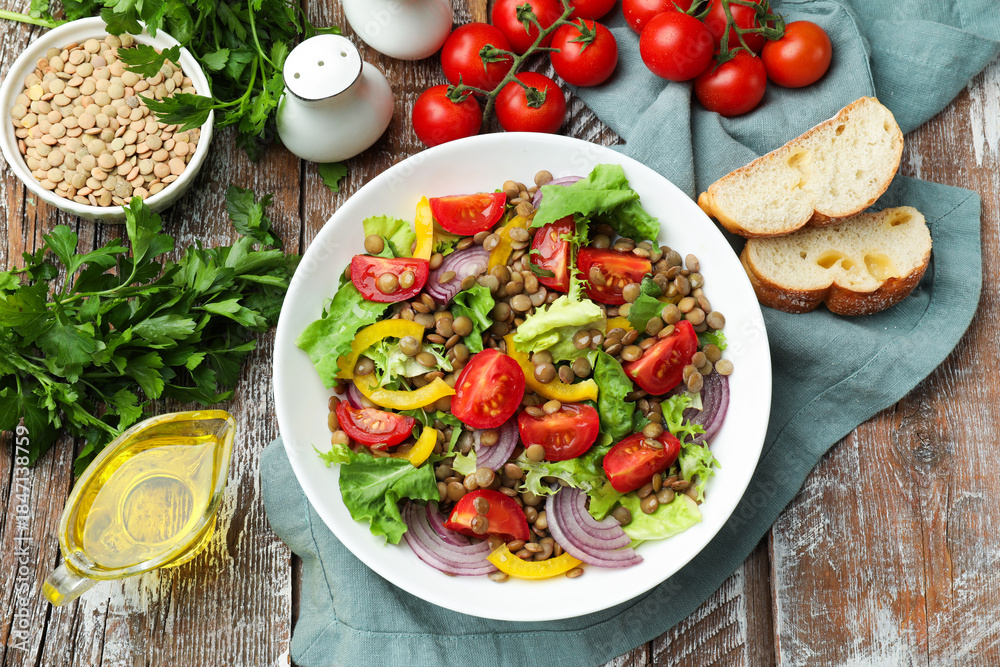Fototapeta premium Delicious lentil salad and ingredients on wooden table, flat lay