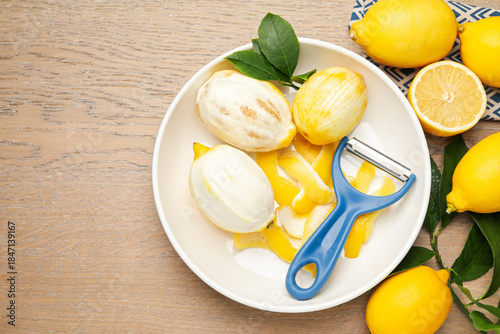 Tableau sur toile Fresh lemons with zest, peeler and leaves on wooden table, flat lay
