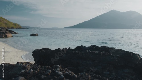 Tropical sea with sandy beach and volcano on the background during sunset