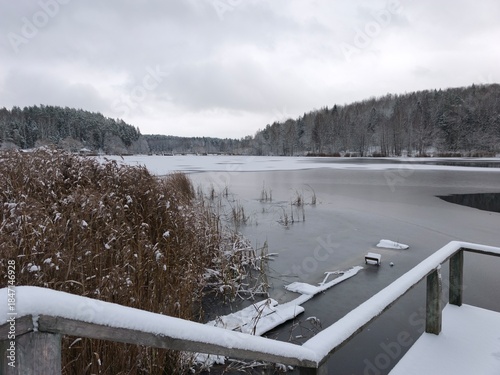 Winter landscape with frozen lake and wooden pier on a cloudy day.